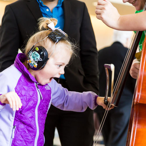 Sensory Friendly Concert. Little Girl with Headphones on enjoys playing with a cello